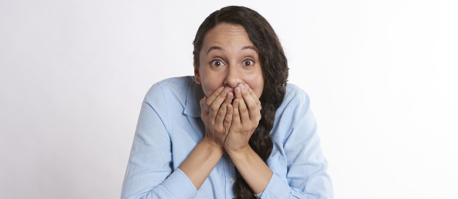 brunette woman with long ponytail, wearing a blue button up shirt, covering her mouth