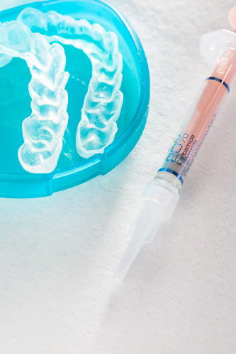 Upper and lower whitening trays sitting in a light blue container next to a syringe of professional-strength whitening gel.