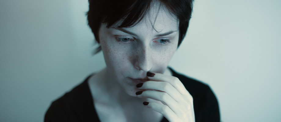 woman with dark short hair looking down, hand on mouth, appearing nervous