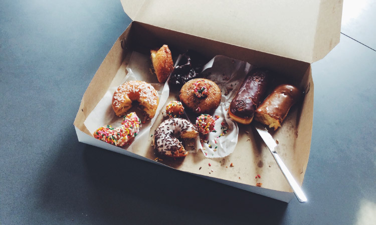 An open cardboard box of half-eaten donuts with chocolate glaze and sprinkles that can cause cavities